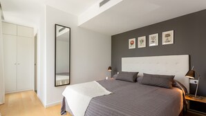 A bedroom with a large bed, a wardrobe, a mirror, and a nightstand with a lamp. - Urban District - Rambla Suites & Pool (Barcelona)