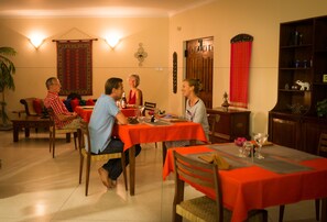 A dining area with a red tablecloth, wooden chairs, and a decorative wall hanging. - Villa 49 (Kandy)