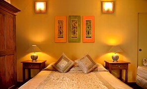 A bedroom with a bed, two bedside tables with lamps, a wooden wardrobe, and three framed artworks on the wall. - Villa 49 (Kandy)