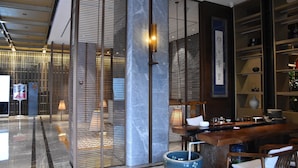 A modern hotel lobby with a reception desk, seating area, and decorative elements like a blue vase and a wall-mounted sign. - Ramada Leshan (Leshan)