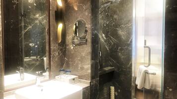 Un baño con lavamanos de mármol, un espejo y zona de ducha.