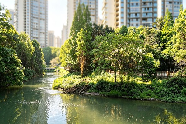 A river with dense greenery and tall buildings in the background. - Ramada Leshan (Leshan)