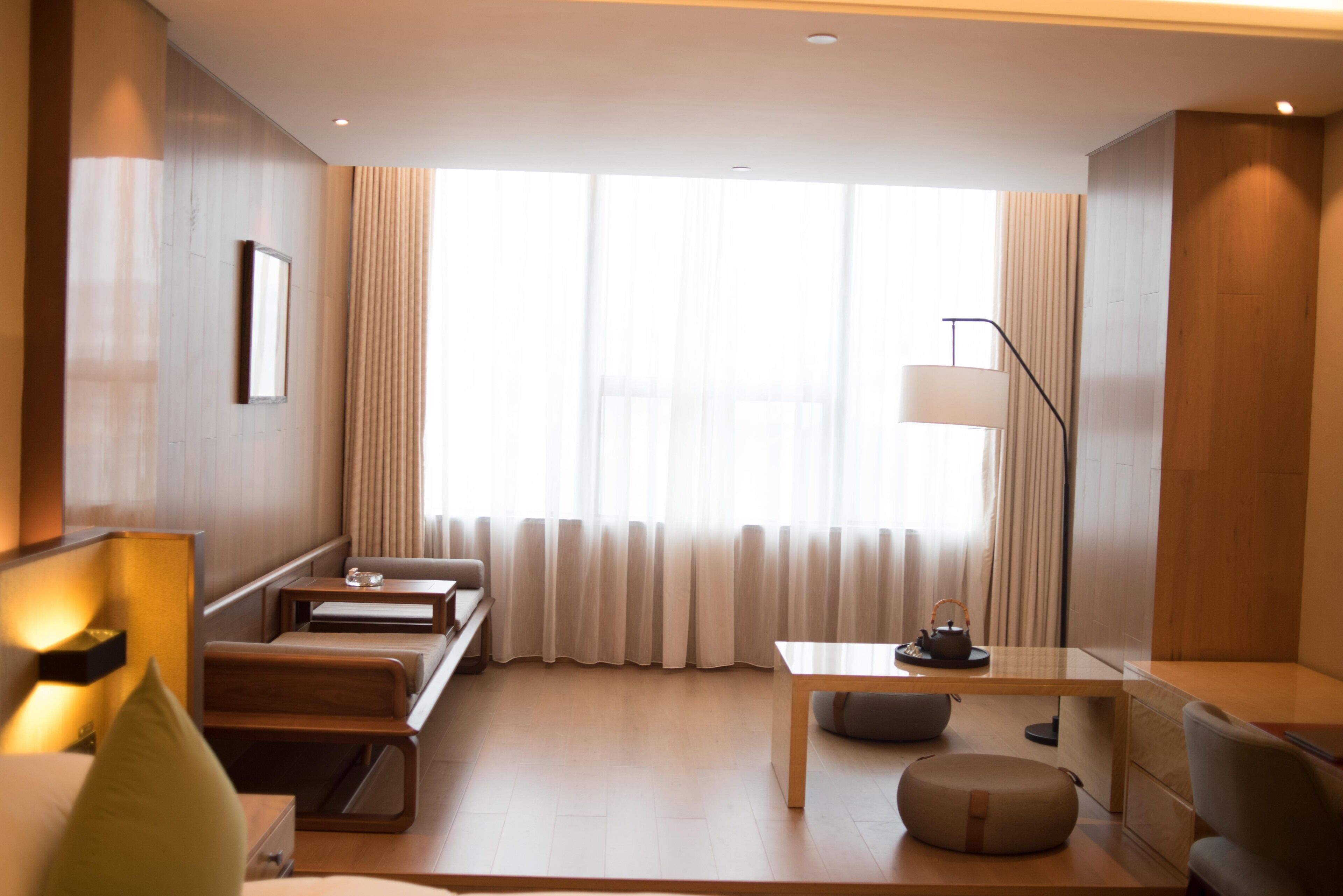 Een moderne hotelkamer met een houten vloer, een bank, een klein tafeltje, een lamp en een raam met gordijnen.