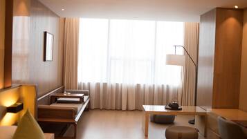 Una habitación de hotel moderna con piso de madera, un sofá, una mesita, una lámpara y una ventana con cortinas.