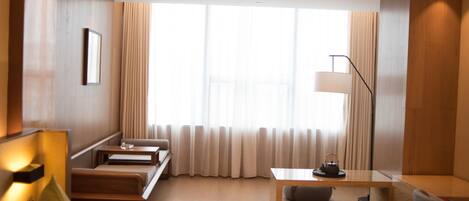 Una habitación de hotel moderna con piso de madera, un sofá, una mesita, una lámpara y una ventana con cortinas.