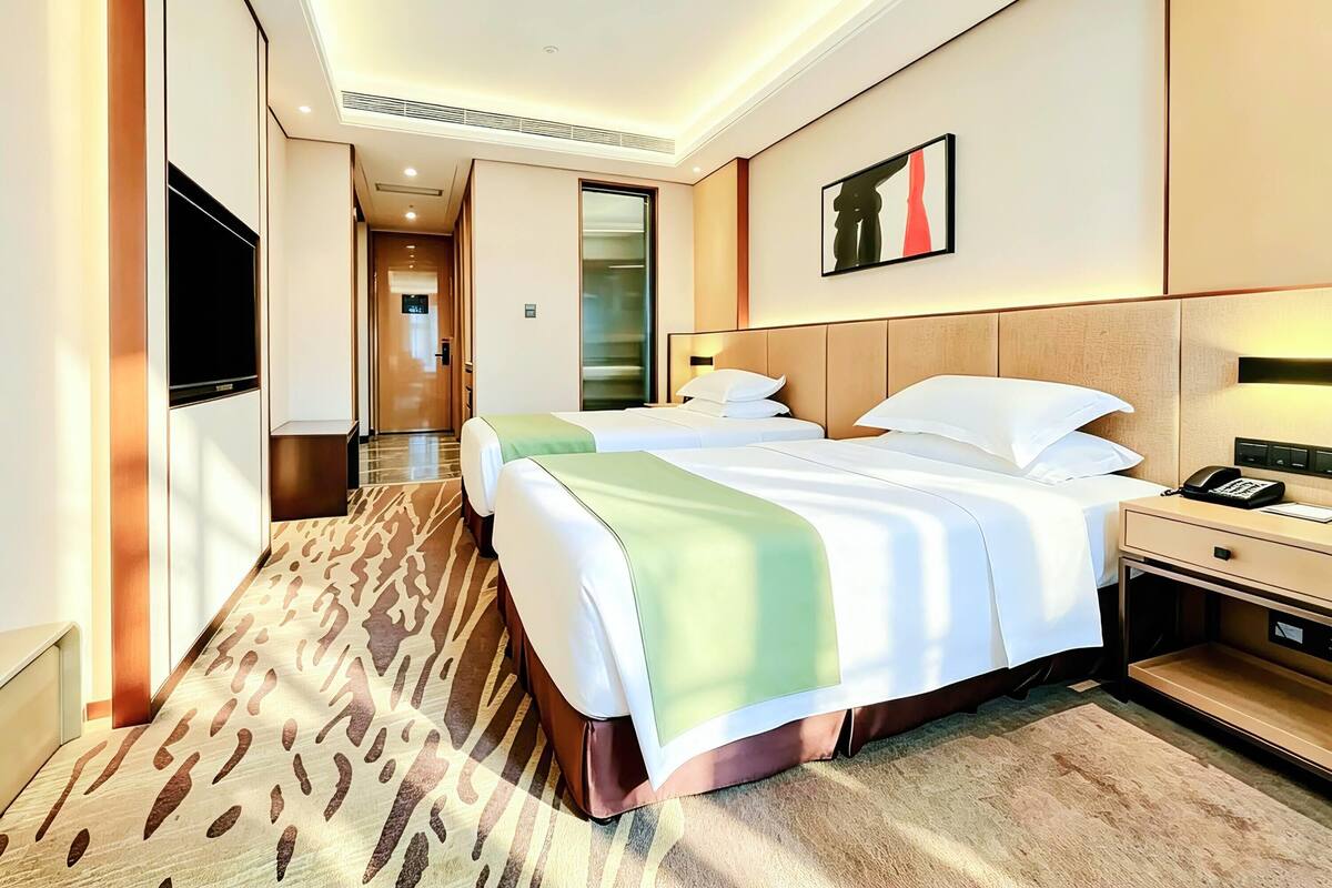 A hotel room with a bed, bedside table, lamp, and a painting on the wall.