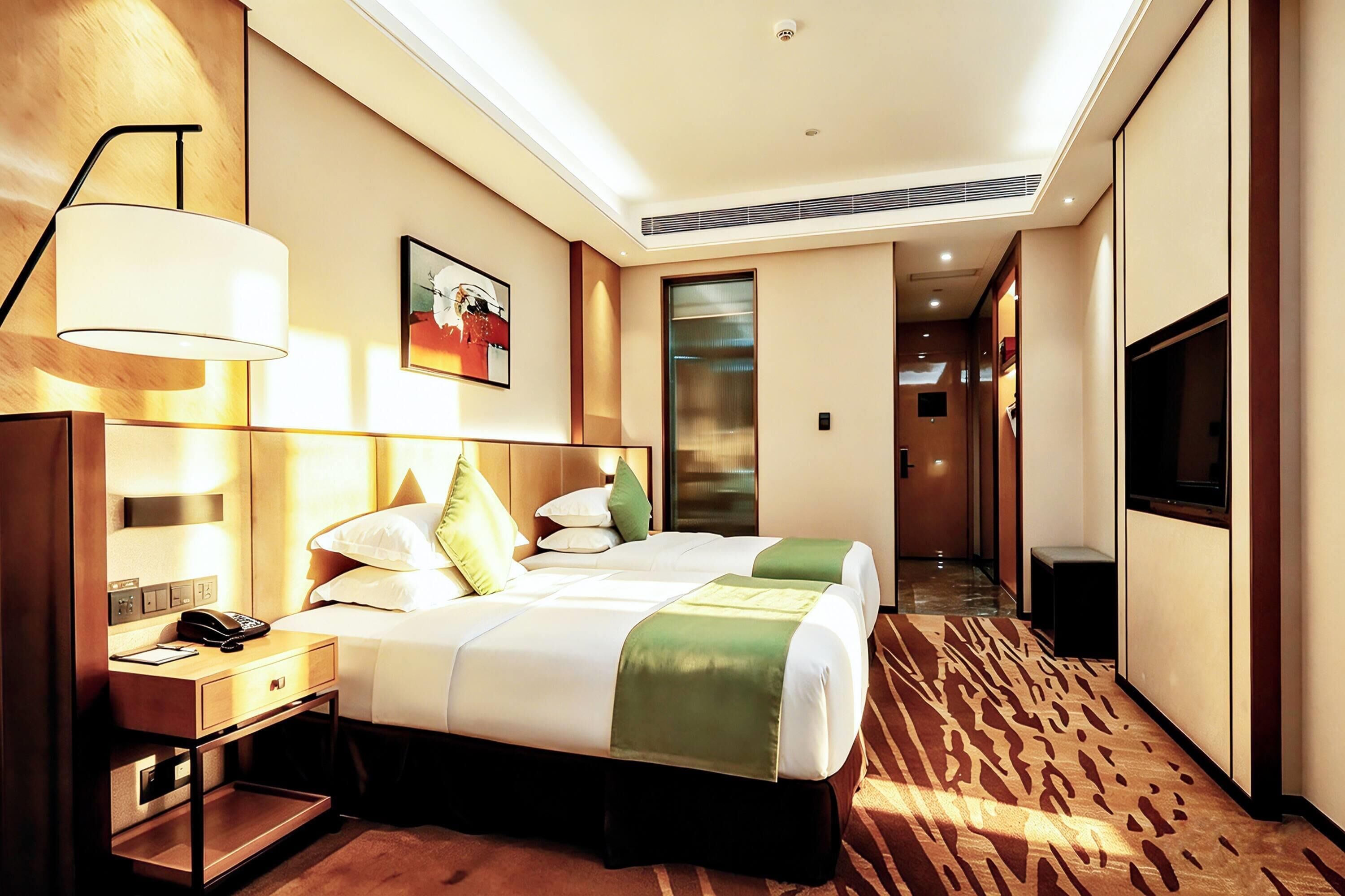 A hotel room with a bed, bedside table, lamp, artwork, and a TV.