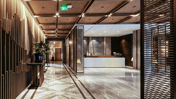 A modern hotel lobby with a reception desk, a plant, and a patterned floor. - Ramada Leshan (Leshan)