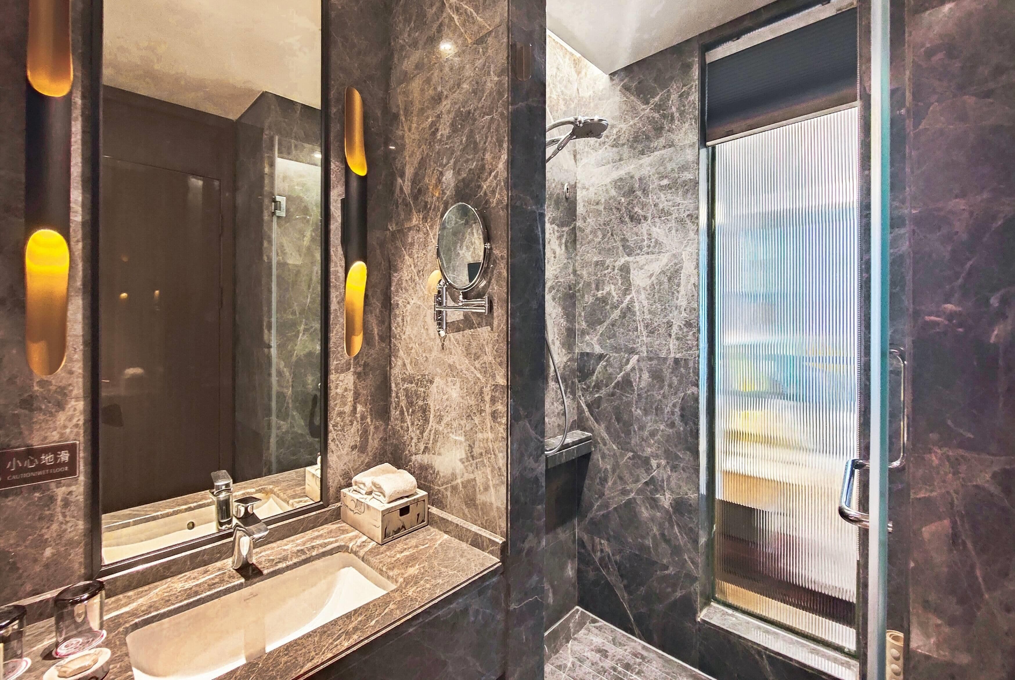 A modern bathroom with a marble sink, a large mirror, and a shower enclosure.