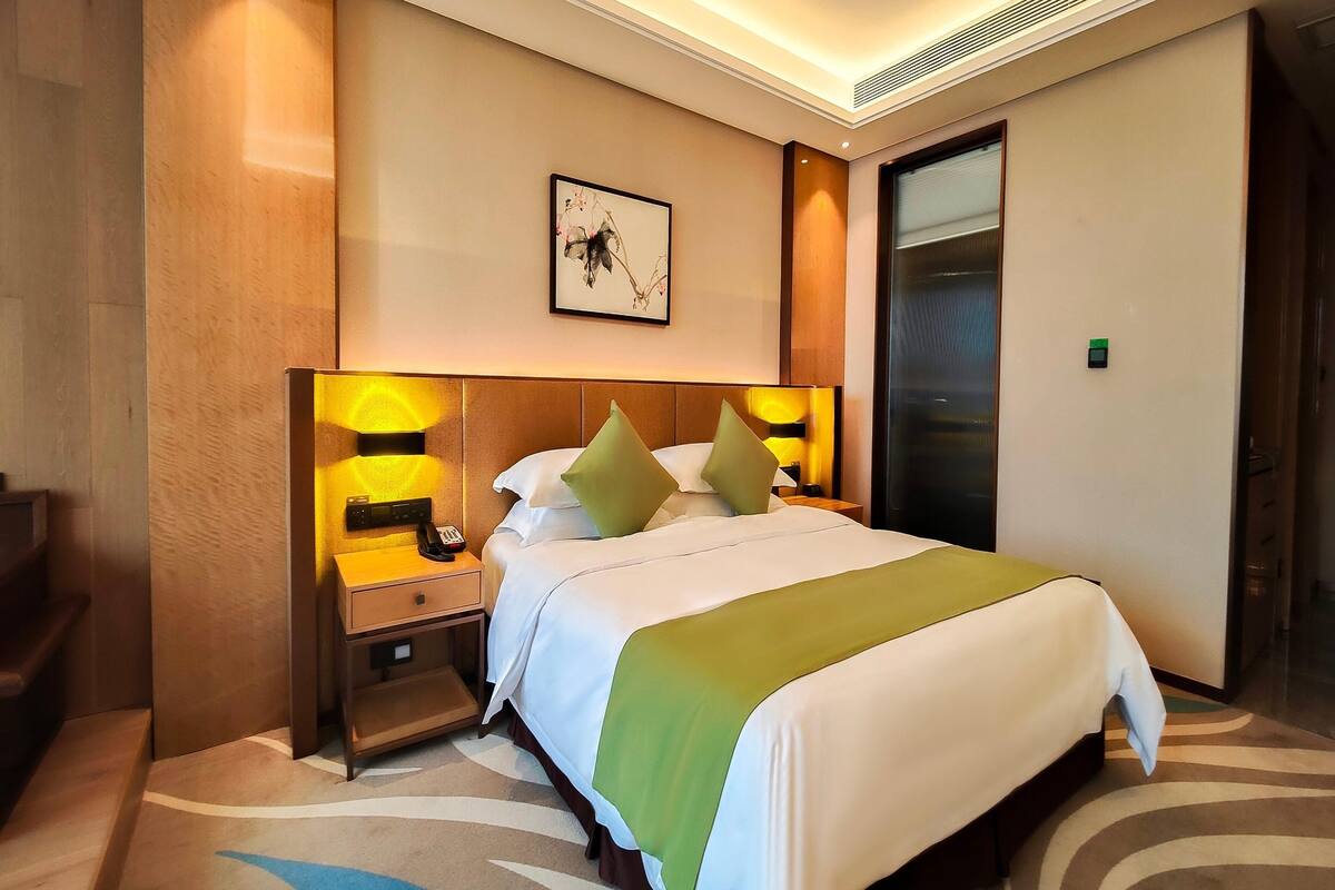 A hotel room with a bed, nightstands, a lamp, a framed picture, and a door.