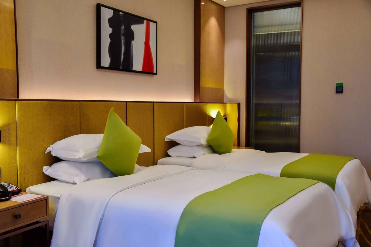 A hotel room with two beds, a nightstand with a phone, and a painting on the wall.