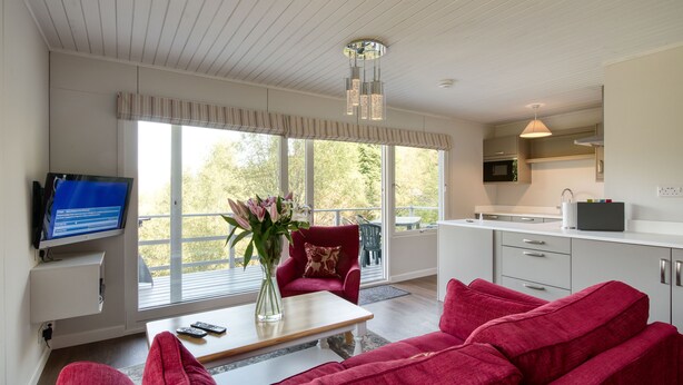 Un salón moderno con un sofá rojo, una mesa de centro y un televisor. Se ve un ventanal con vistas a árboles.