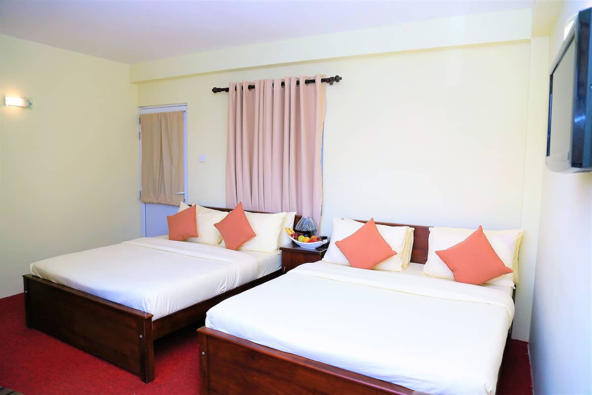 Quarto de hotel com duas camas de solteiro, cada uma com estrutura de madeira e roupa de cama branca. Há uma mesa de cabeceira com uma cesta de frutas e uma luminária entre as camas.