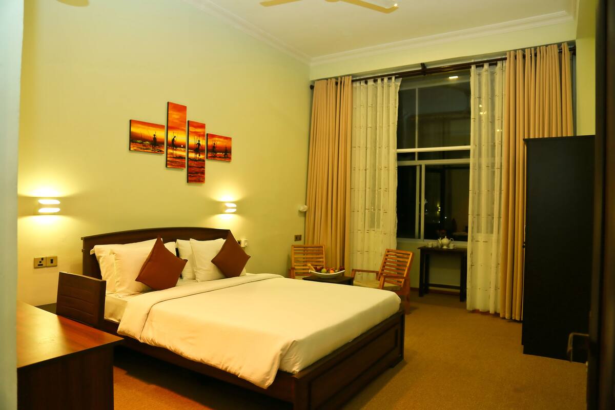 Quarto de hotel com uma cama grande, uma escrivaninha, duas cadeiras, uma mesa de jantar e uma televisão.
