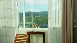 A room with a view of a green landscape through a window, a wooden chair, and a small table with a teapot and cups. - Lourdes Hotel (Nuwara Eliya)