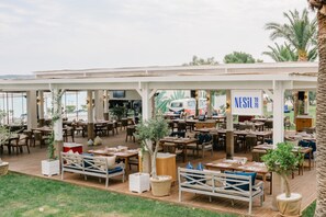 Enjoy casual dining under a shaded roof with comfortable seating and lush greenery.