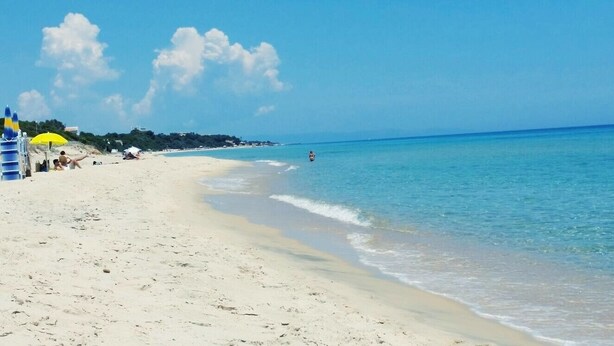 Ein Strand mit blauem Himmel, sandigem Ufer und einigen Sonnenschirmen.