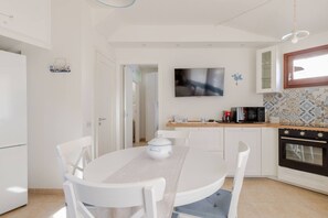 Kompakti keittiö, jossa on ruokapöytä, valkoiset tuolit, televisio, mikroaaltouuni ja liesi.