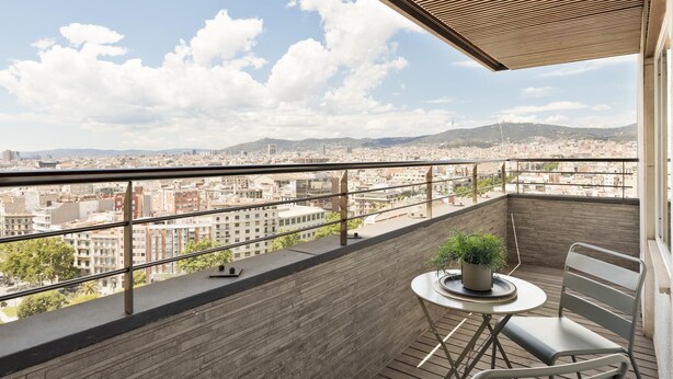 A balcony with a view of a cityscape, a round table with a potted plant, and two chairs. - Amazing skyline with amazing views (Barcelona)