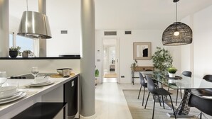 A modern kitchen with a central island, pendant lights, and a dining area with a glass table and chairs. - Amazing skyline with amazing views (Barcelona)