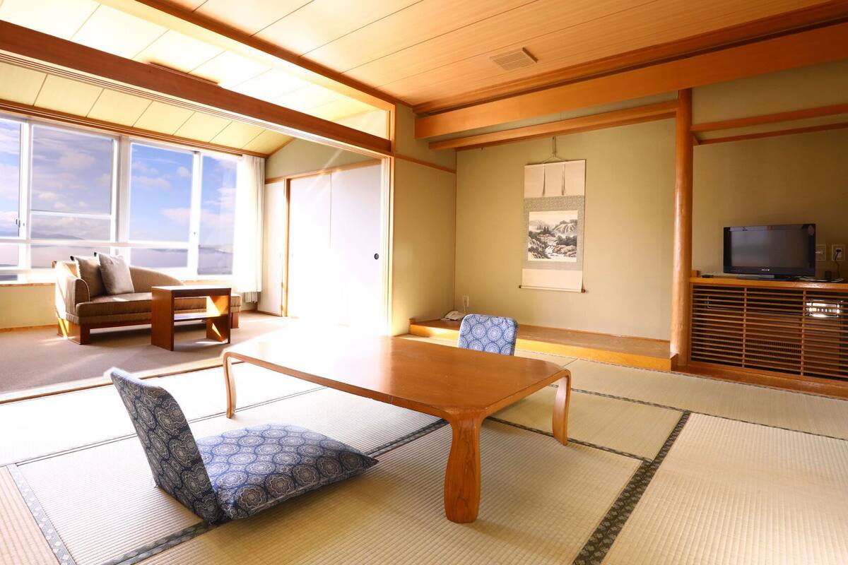 Una habitación japonesa tradicional con suelo de tatami, una mesa baja, un sofá y un televisor sobre un mueble de madera.