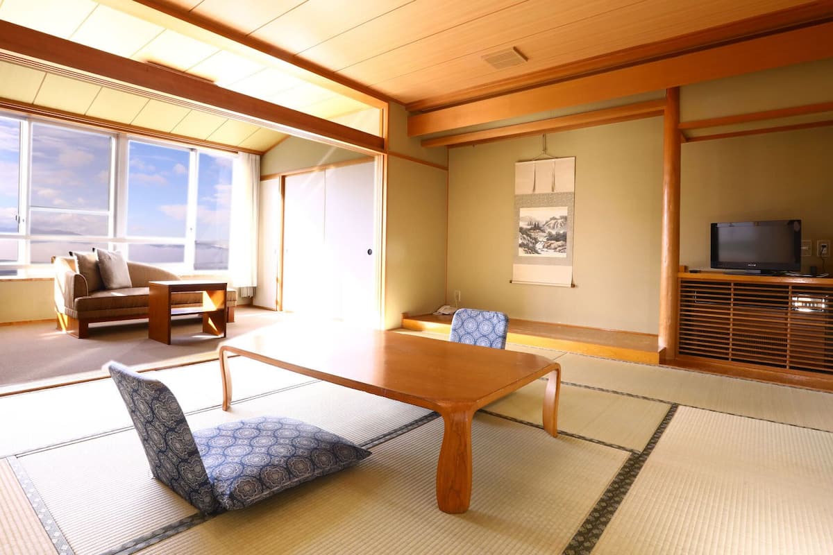 A traditional Japanese room with tatami flooring, a low table, a sofa, and a television on a wooden stand.