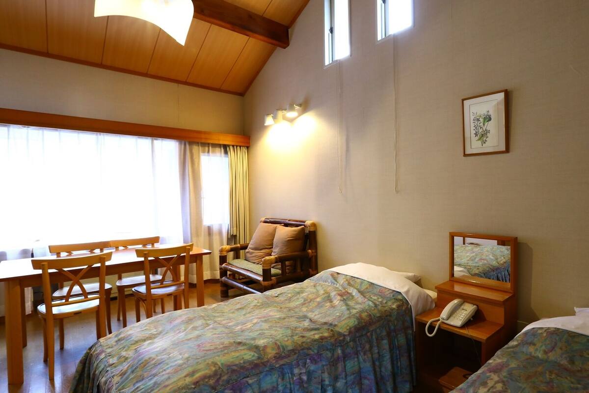 Habitación de hotel con dos camas, un escritorio, una silla, un teléfono y un cuadro en la pared.