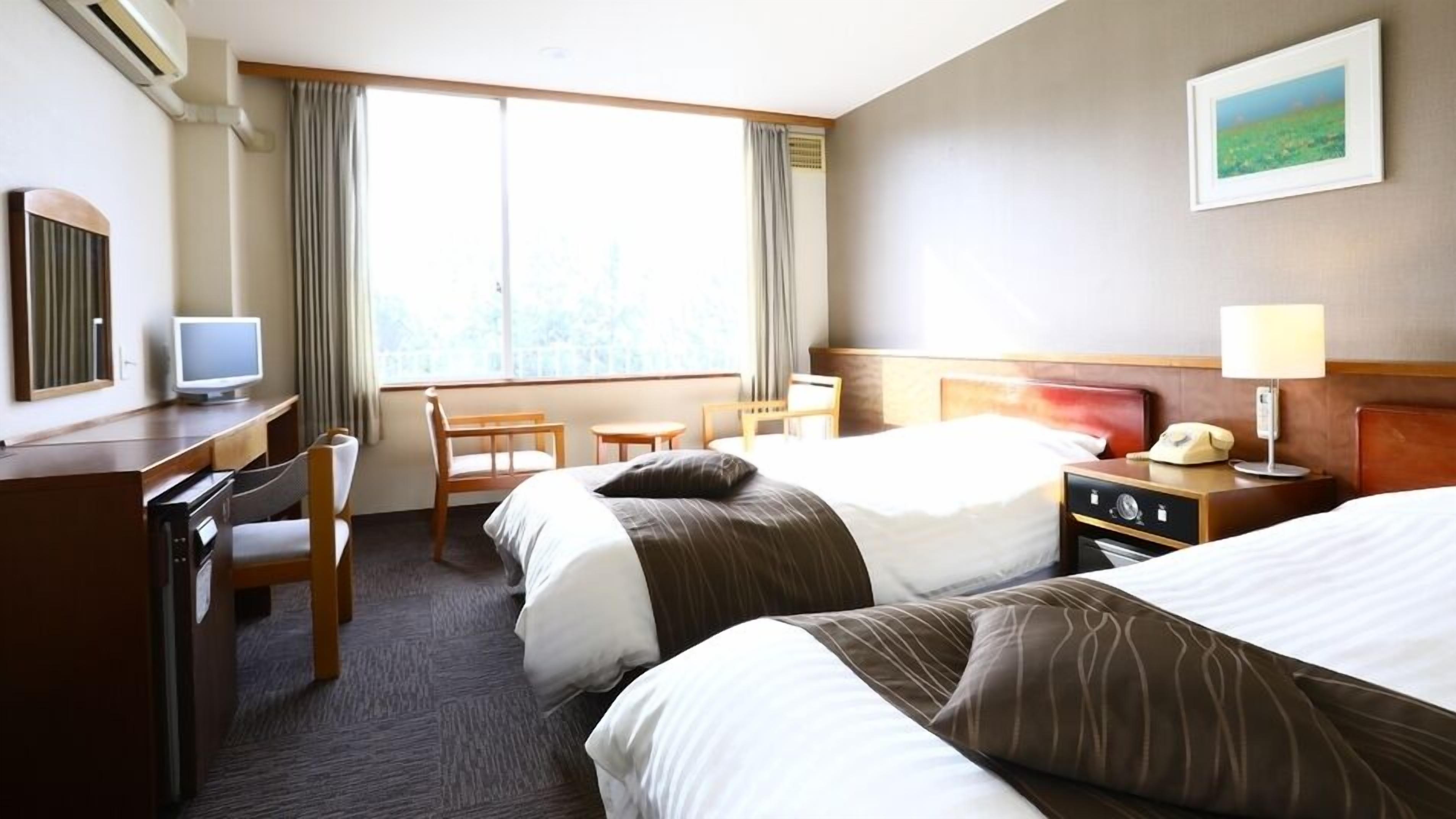 A hotel room with two beds, a desk with a computer, a chair, a TV, and a window with curtains.