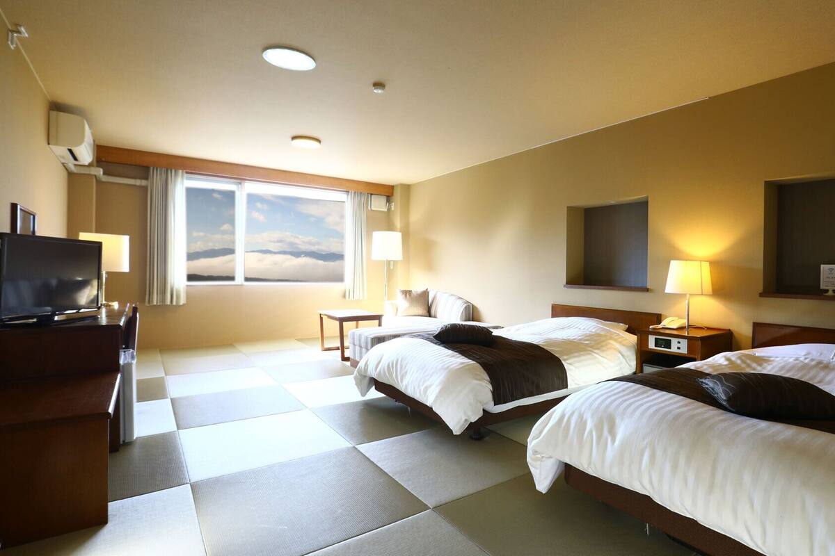 Habitación de hotel con dos camas, televisión, escritorio y ventana con vista al cielo.