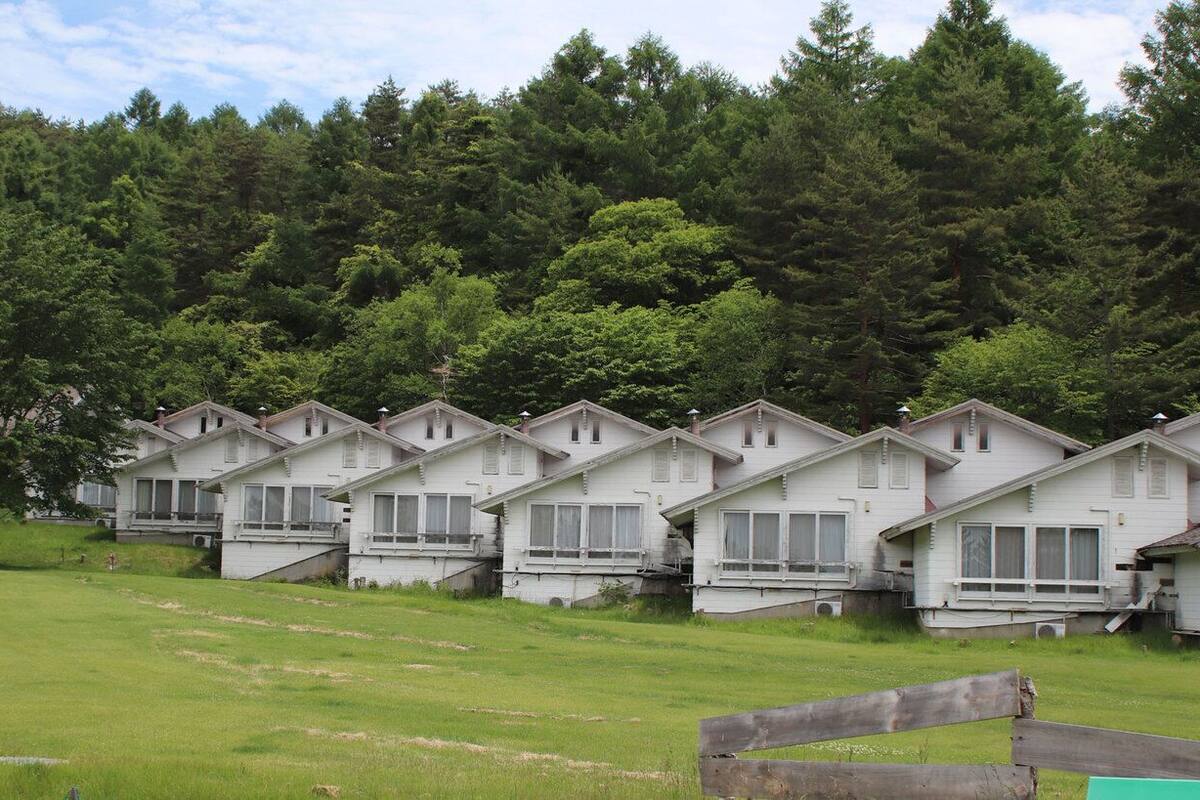 Una hilera de cabañas blancas con balcones, con un denso bosque de fondo.