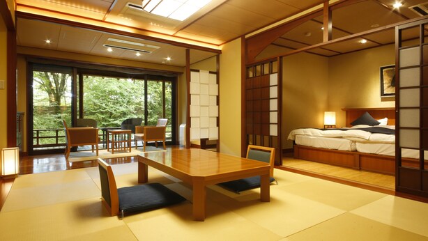 A traditional Japanese-style room with tatami flooring, a wooden table, and a bed with a futon. - Tateshina Ai (Chino)