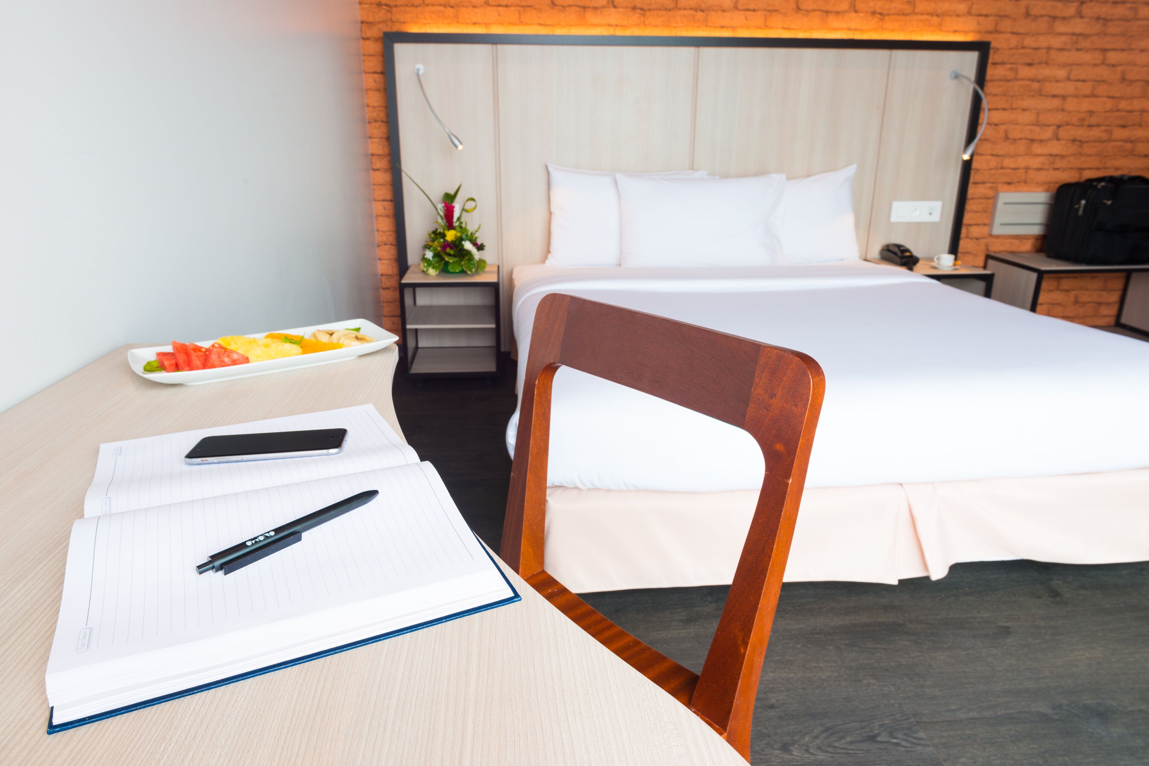Une chambre d’hôtel avec un lit, un bureau avec un carnet, un stylo, un téléphone intelligent et une assiette de fruits.