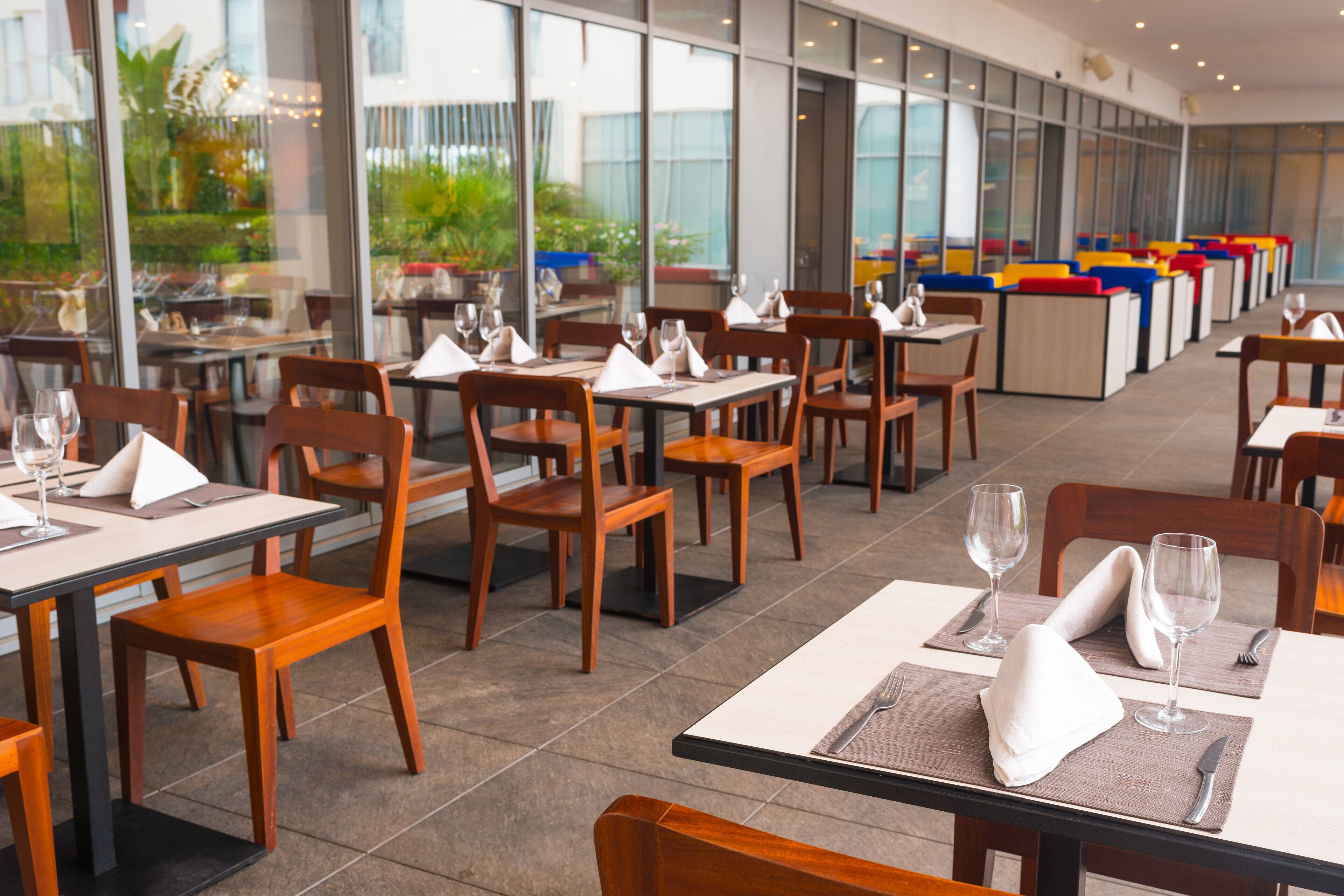 Un restaurant modern amb taules i cadires de fusta, distribuïdes en un espai ampli i amb grans finestres que donen vista a la vegetació.