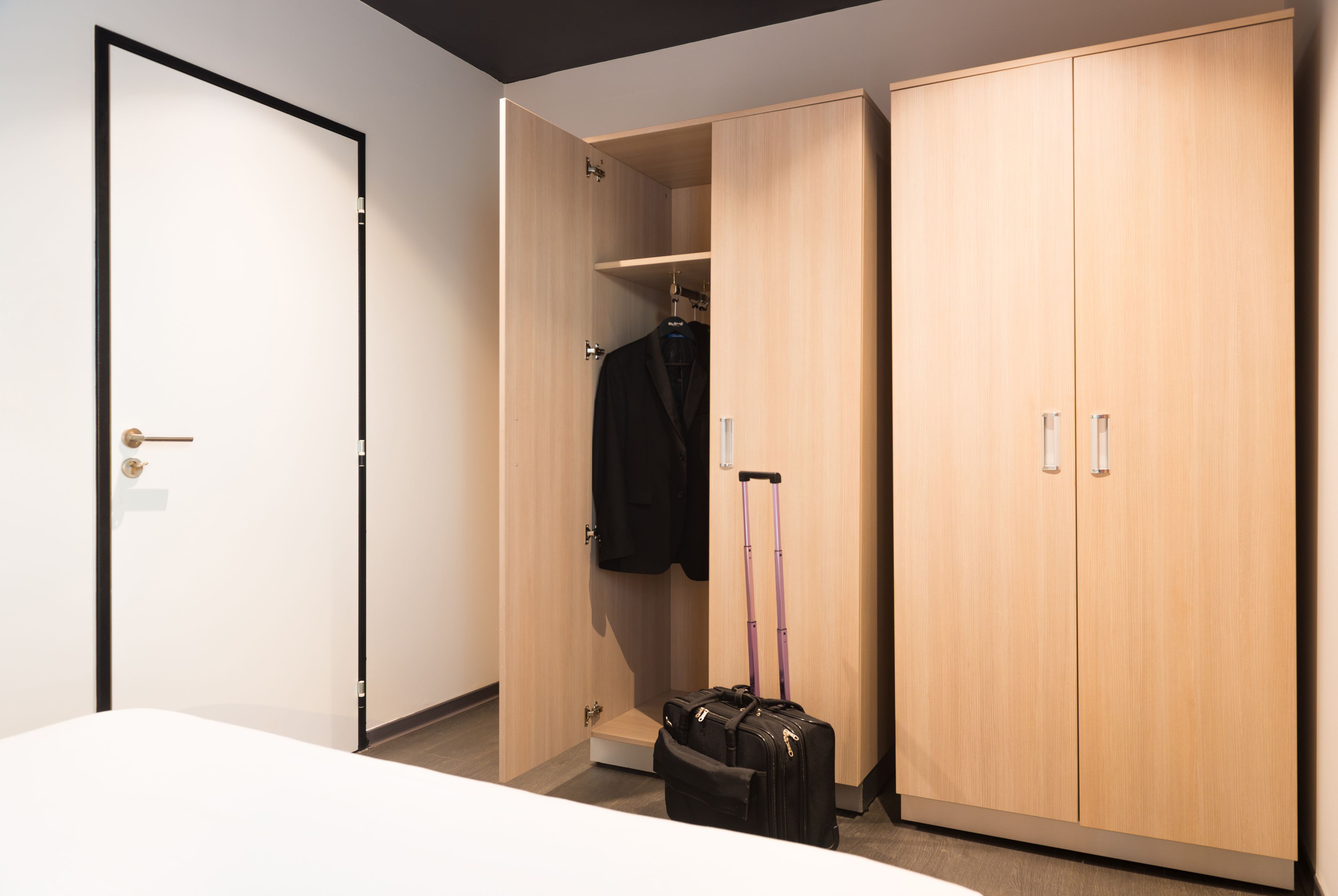 A hotel room with a wardrobe, a bed, and a suitcase.