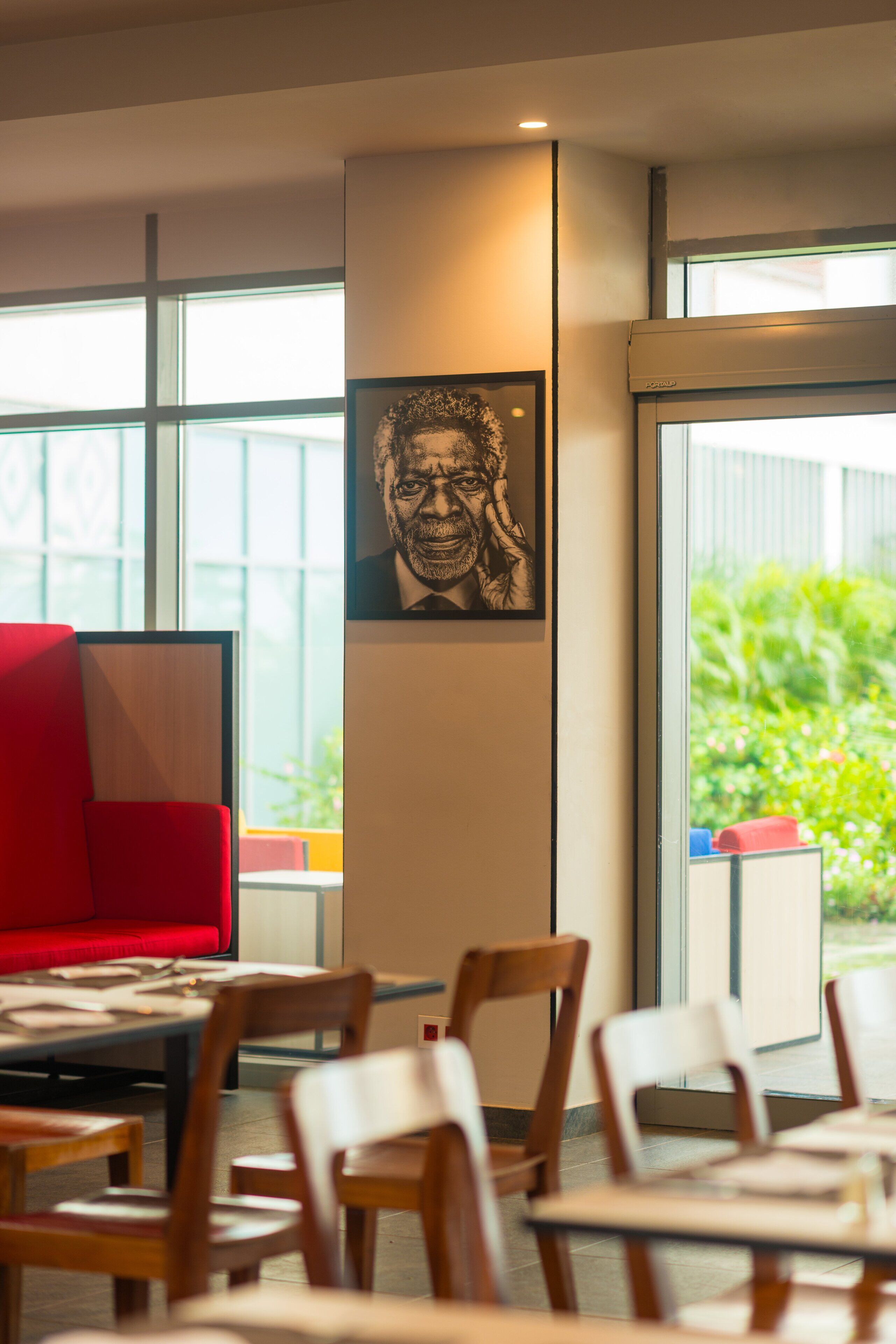 A modern interior with a red sofa, wooden chairs, a table, and a framed artwork on the wall.
