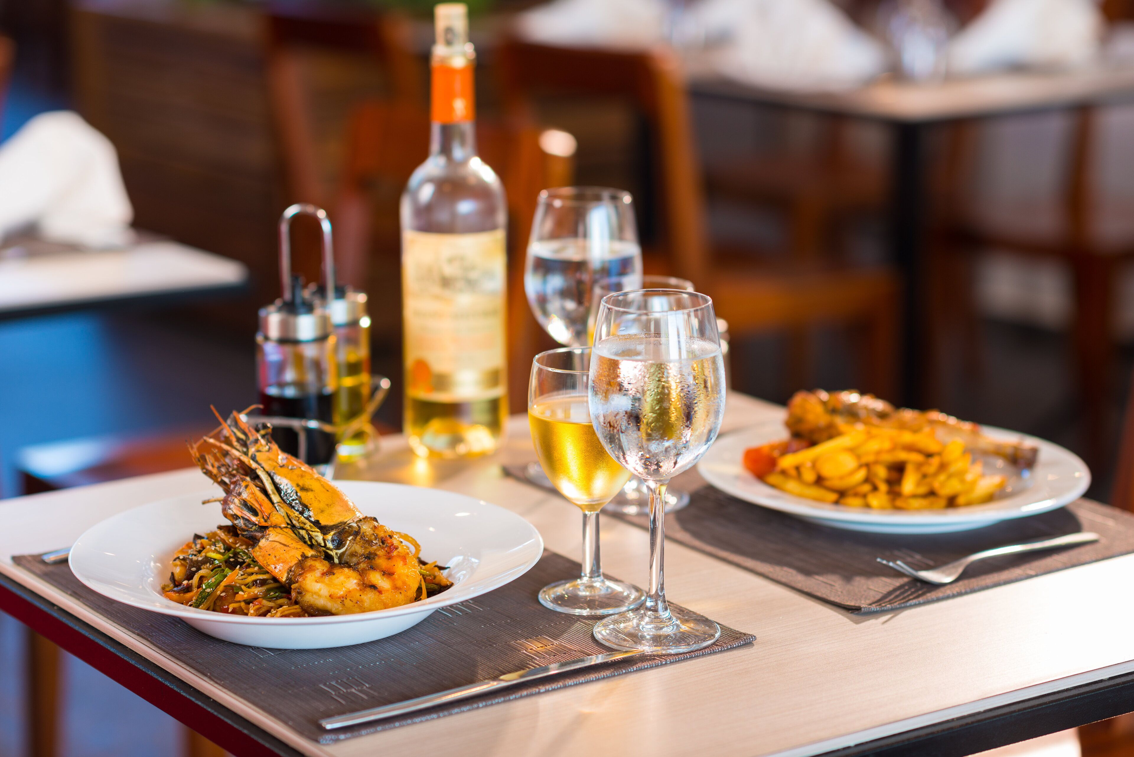 A dining table with two plates of food, a bottle of wine, and two wine glasses.