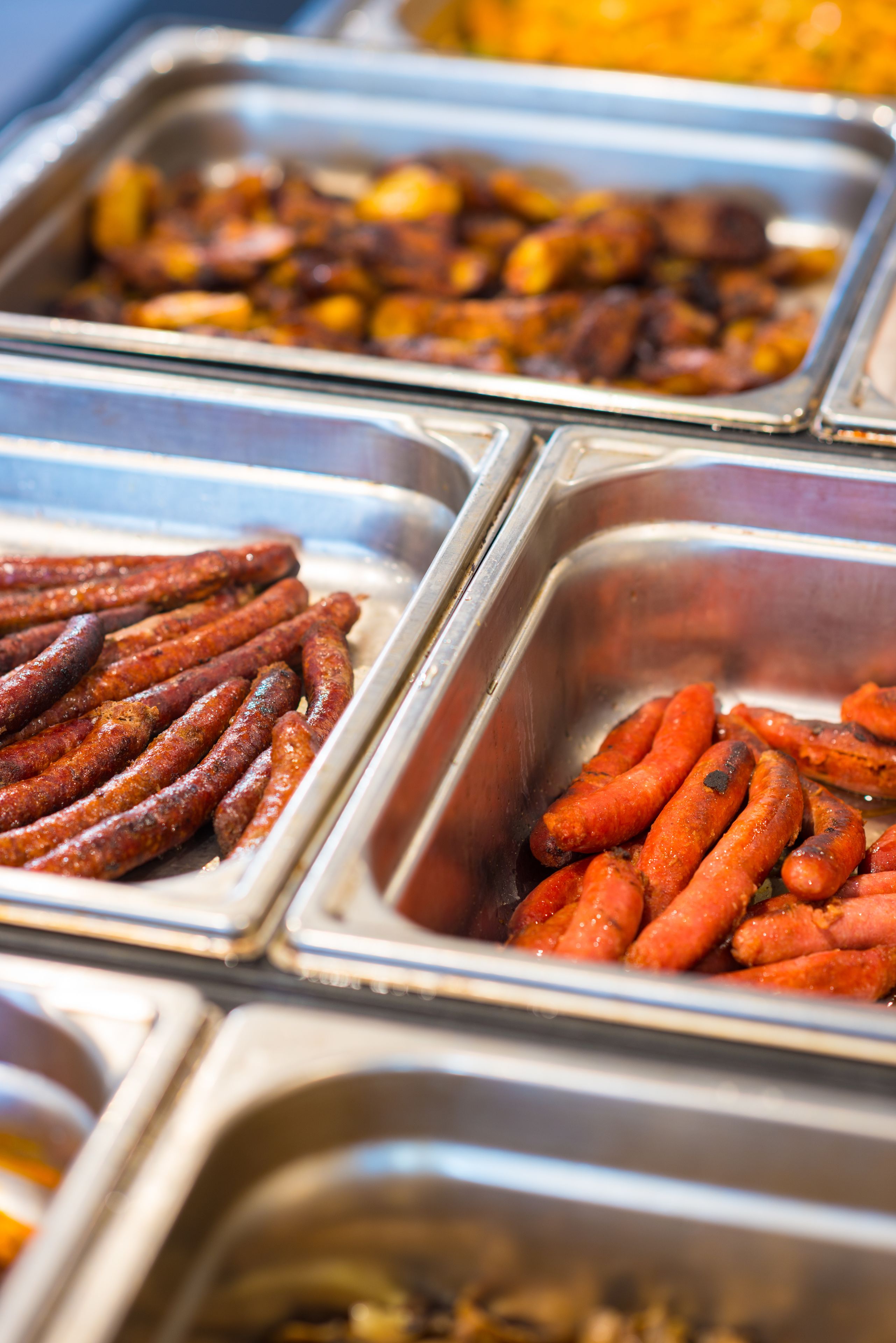 Buffet com diversos alimentos, incluindo salsichas e batatas assadas.