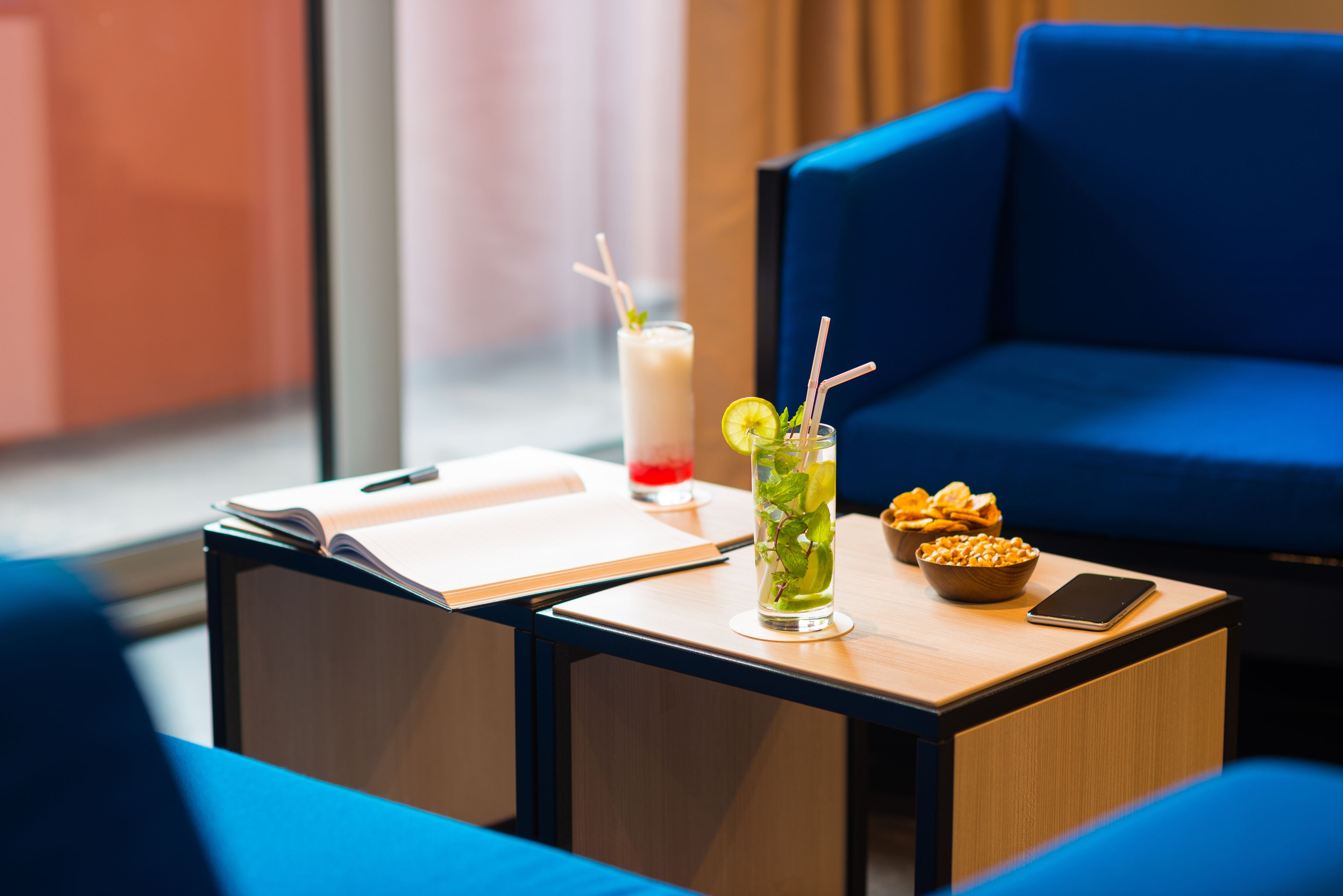 A modern lounge area with a blue sofa, a small wooden table with a drink, snacks, and a smartphone.