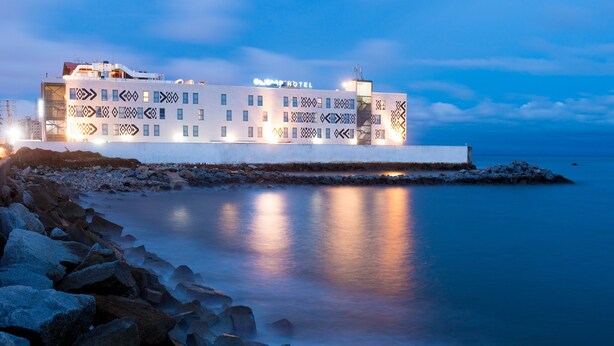Et hotel med moderne design, karakteriseret ved en geometrisk facade og beliggenhed ved vandet.
