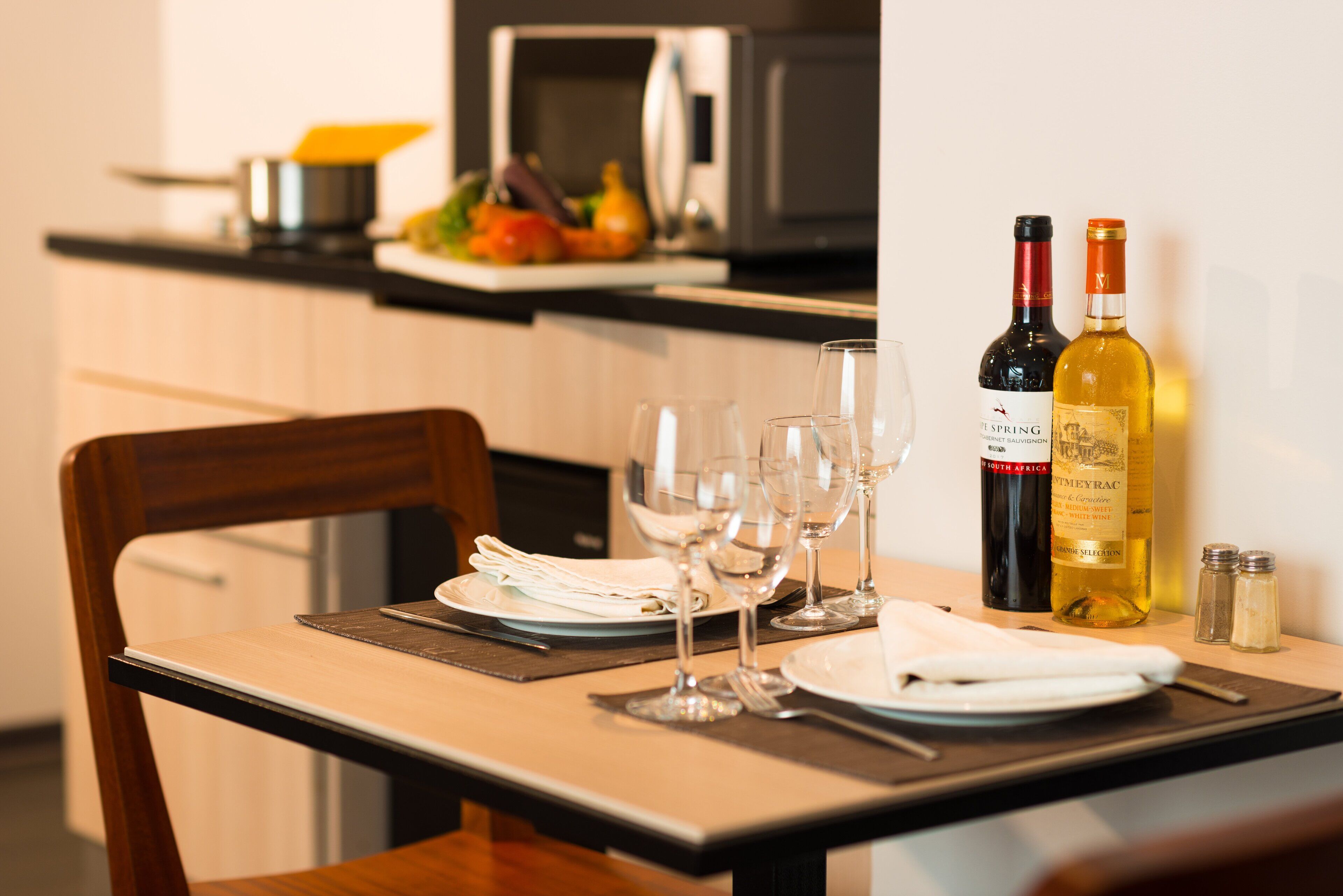 A dining table set with plates, glasses, and cutlery, with two wine bottles and salt shakers on the table.
