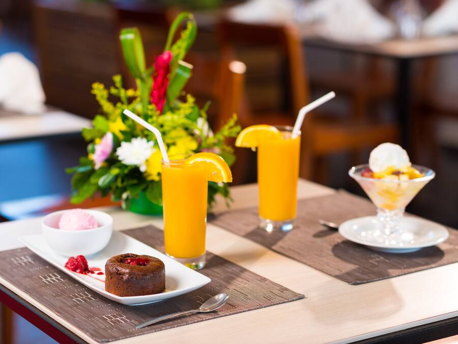 A dining table with a dessert plate, two glasses of orange juice, a bowl of ice cream, and a floral centerpiece.