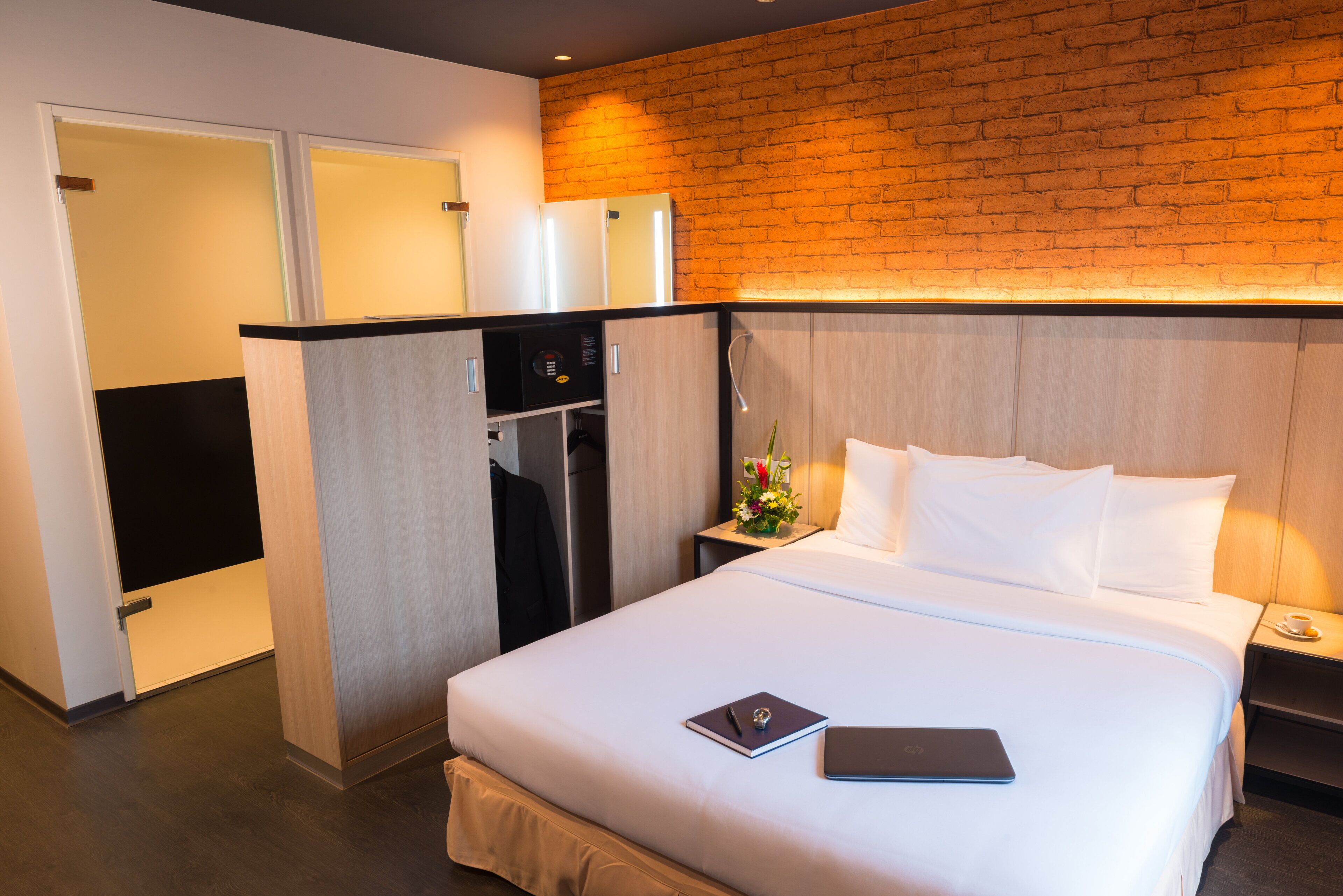 A hotel room with a bed, a desk, a microwave, and a brick wall.
