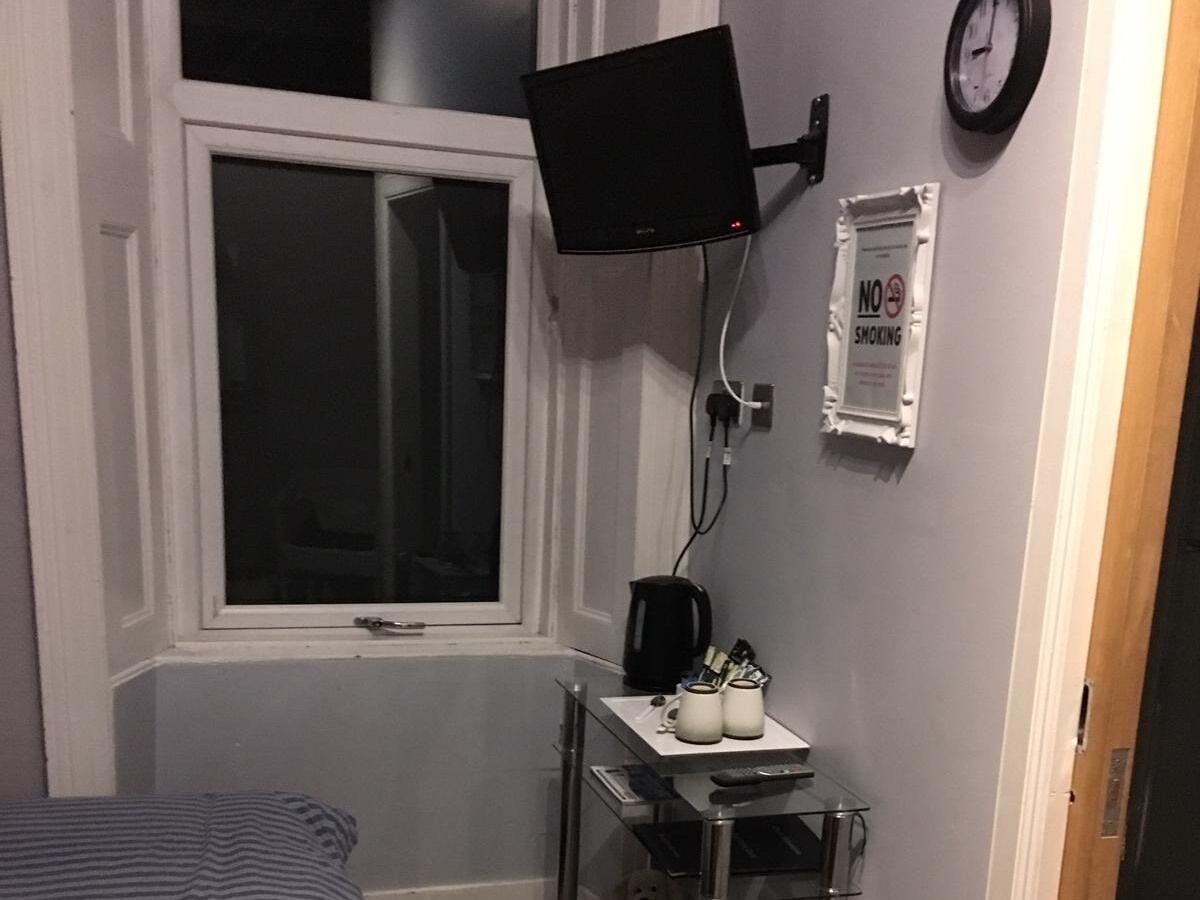 Een kamer met een raam, een wandgemonteerde flatscreen-tv, een koffiezetapparaat en een klein tafeltje met bekers en een afstandsbediening.