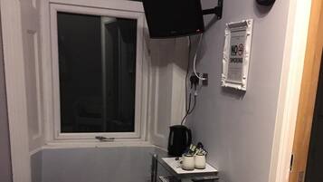 Een kamer met een raam, een wandgemonteerde flatscreen-tv, een koffiezetapparaat en een klein tafeltje met bekers en een afstandsbediening.
