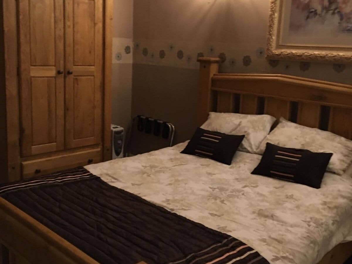Een slaapkamer met een houten bed, twee kussens, een nachtkastje en een kledingkast.