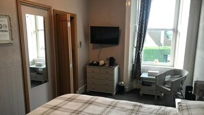 A hotel room with a bed, a dresser, a television, a chair, and a window with curtains. - Macbeth Arms (Banchory)