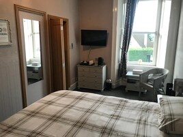 A hotel room with a bed, a dresser, a television, a chair, and a window with curtains.
