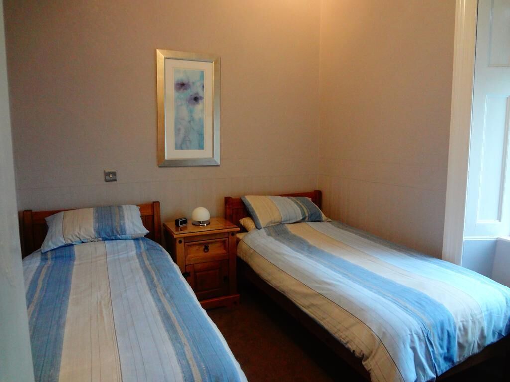 Una habitación con dos camas individuales, una mesita de noche con lámpara y un cuadro enmarcado en la pared.