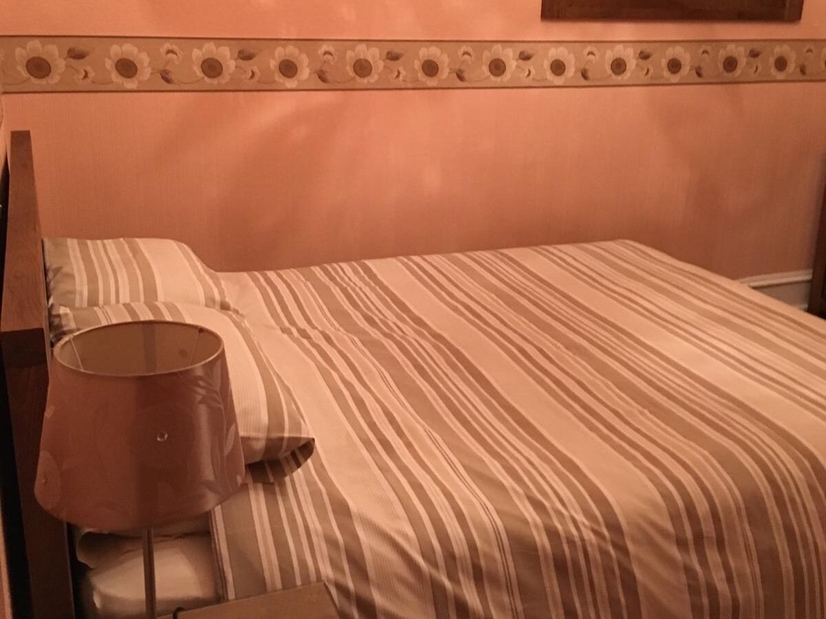 Una cama con ropa de cama a rayas, una almohada y una lámpara en una mesita de noche.