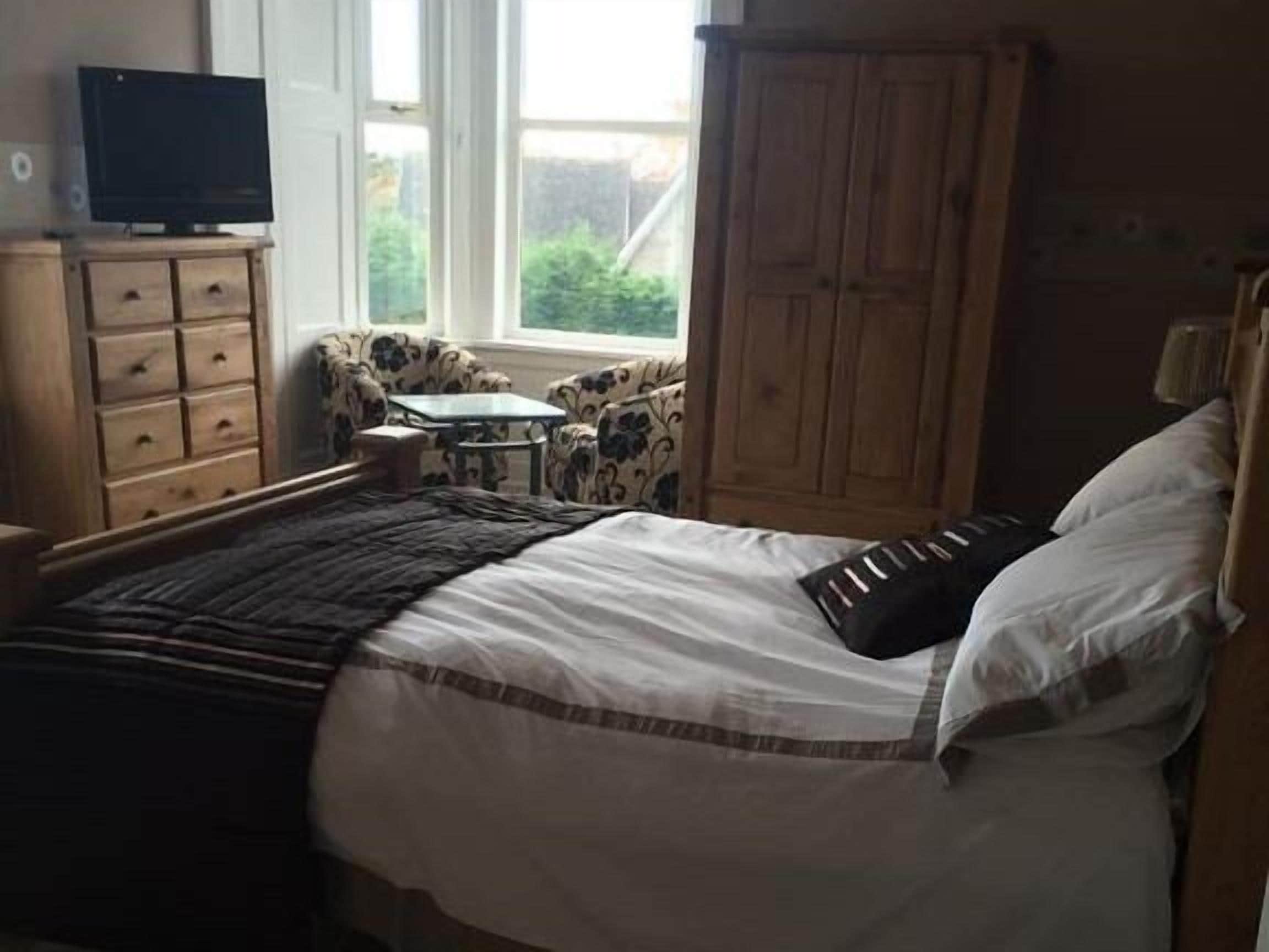Un dormitorio con una cama, un televisor sobre un mueble de madera, una mesita y una silla.